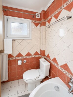 Ein Badezimmer mit Toilette, Bidet, Badewanne und einem Fenster.
