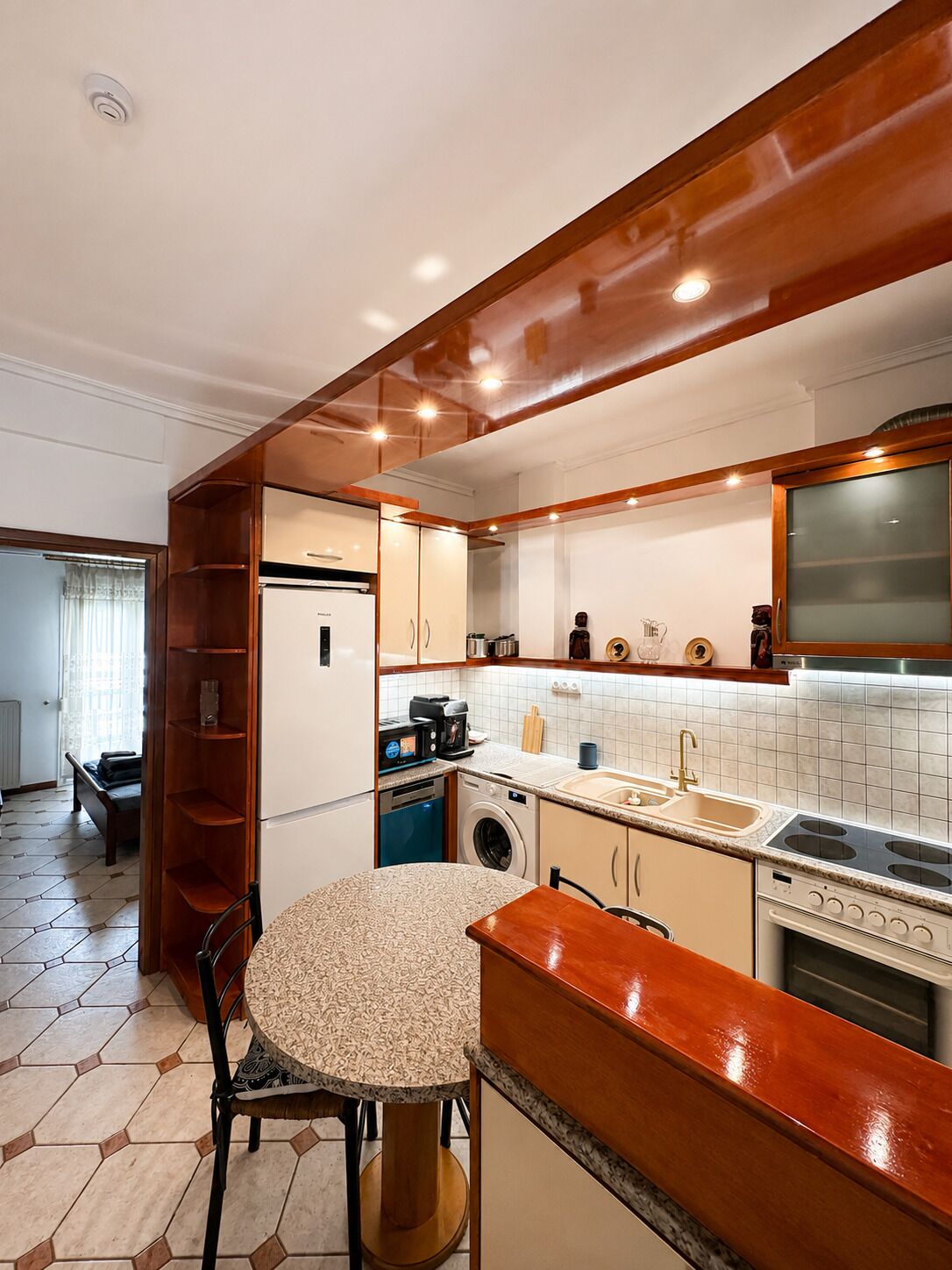 Une cuisine compacte avec une table de salle à manger ronde, des appareils électroménagers intégrés et un mur d’accent en bois.
