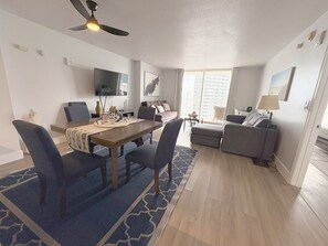 Ein modernes Hotelzimmer mit Essbereich, einer Couch, einem Fernseher und einem großen Fenster.