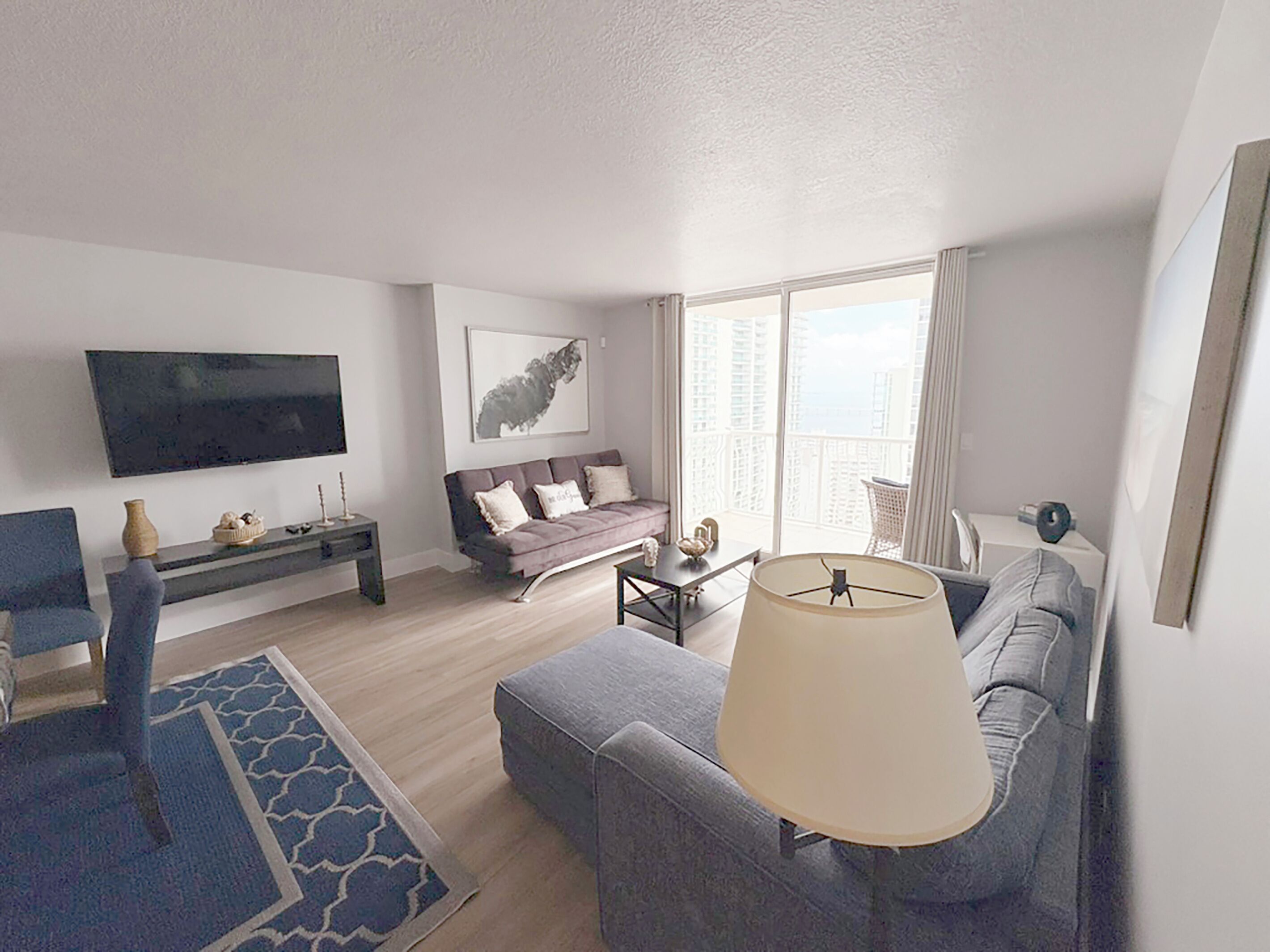 A modern living room with a sofa, a coffee table, a TV, and a large window offering a view of buildings.
