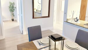 A dining area with a table set for four, a mirror on the wall, and a potted plant in the corner.