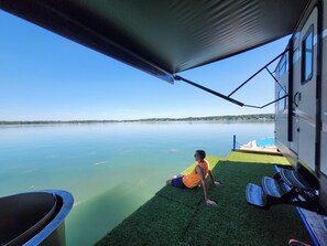 A person on a grassy platform with a view of a calm lake and a boat dock.