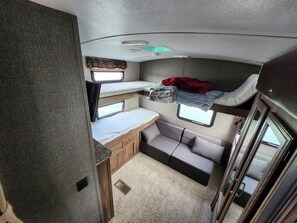 A compact RV interior with a bunk bed, a small kitchenette, and a seating area.