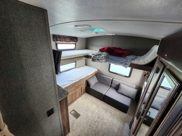 A compact RV interior with a bunk bed, a small kitchenette, and a seating area.