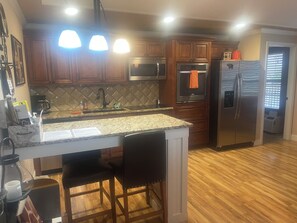 Eine Küche mit Holzschränken, einer Arbeitsplatte aus Granit, einem Edelstahlkühlschrank und einem eingebauten Backofen.