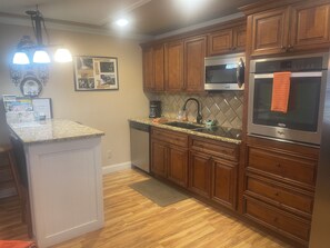 A kitchen with wooden cabinets, a granite countertop, a stainless steel refrigerator, and a microwave. - JAMBO @ Cades Cove Landing Unit 110 (Townsend)