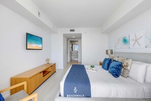 Ein modernes Schlafzimmer mit einem großen Bett, einem Holzkonsolentisch, einem Fernseher und Kunstwerken an den Wänden.