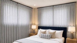 Quarto de hotel com uma cama grande, duas mesas de cabeceira com luminárias e cortinas pesadas.