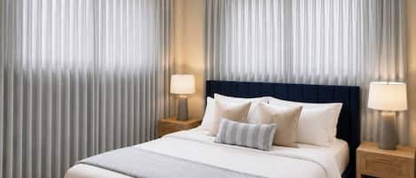 A hotel room with a large bed, two bedside tables with lamps, and heavy drapes.