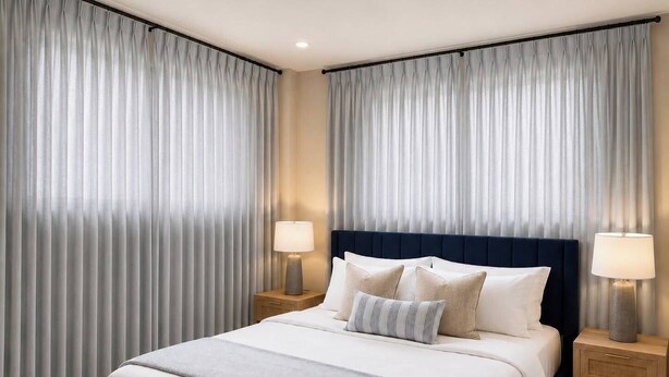 Quarto de hotel com uma cama grande, duas mesas de cabeceira com luminárias e cortinas pesadas.