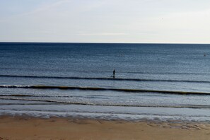 A beach with waves, a person in the water, and a distant buoy.