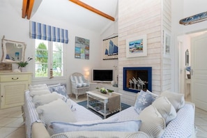 A cozy living room with a sofa, TV, and fireplace. - Joli Villa | Proche de la plage + Parking Gratuit (St Jean de Monts – France)