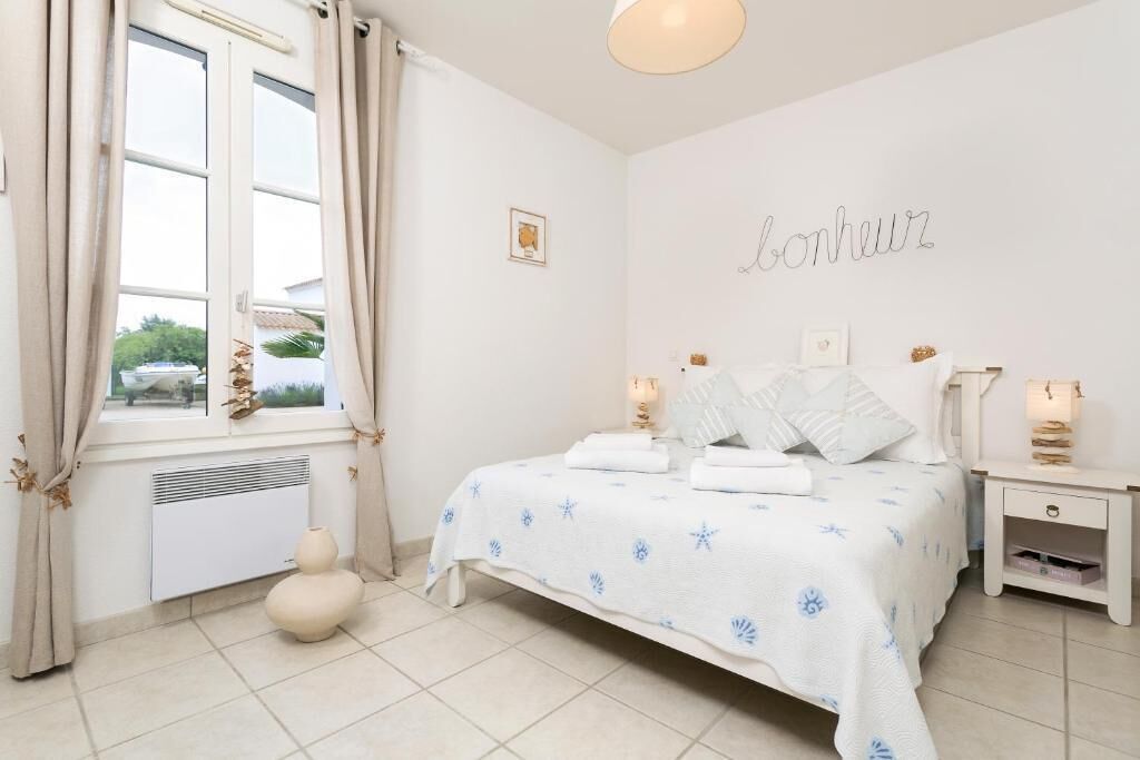 Un dormitorio con cama, mesitas de noche, una ventana con cortinas, un radiador y una pared con un cartel.
