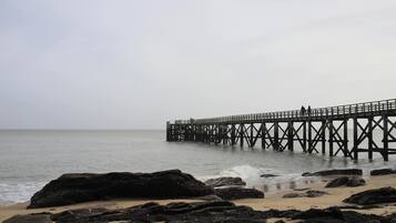 Un muelle se adentra en aguas tranquilas, rodeado de rocas y una playa de arena.