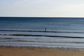 Ein Strand mit Wellen, eine Person im Wasser und ein weiter entfernt liegender Boje.