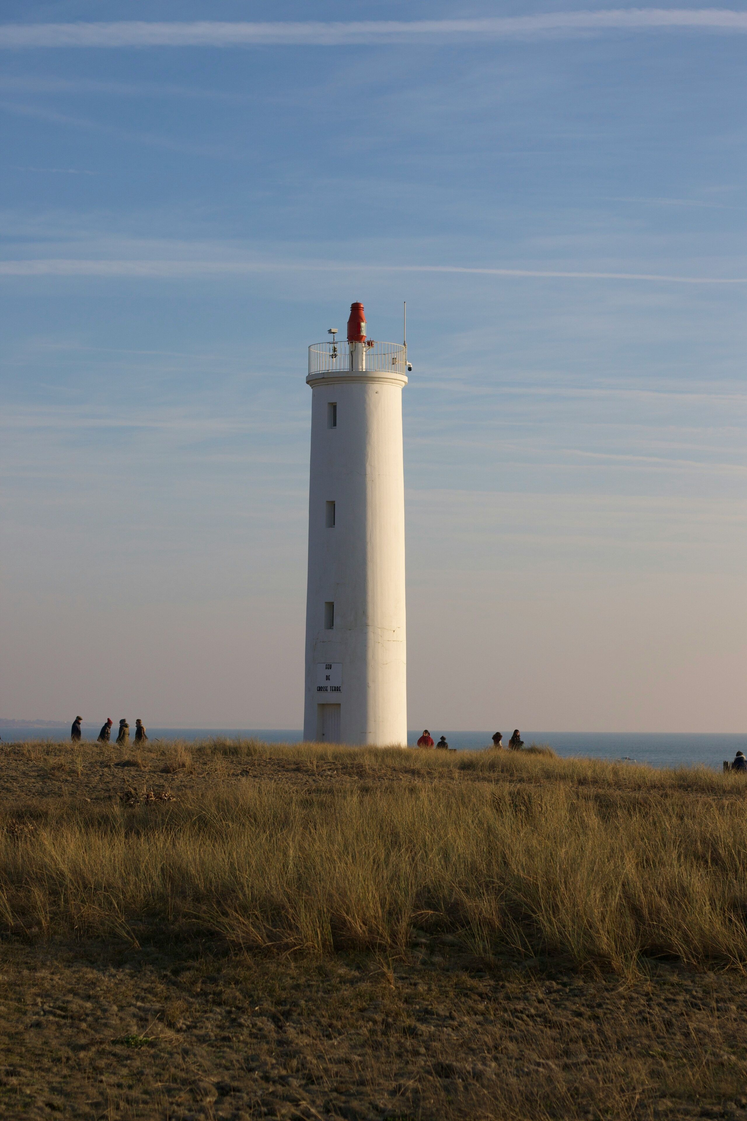 Un faro con cielo despejado, ubicado en un campo cubierto de hierba y algunas personas a lo lejos.
