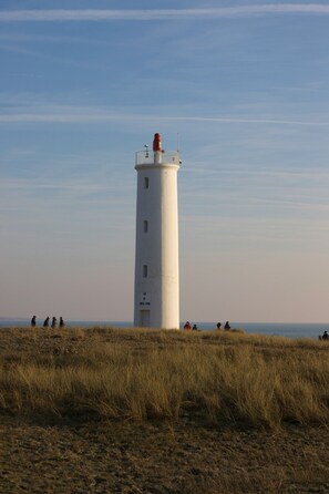 A lighthouse with a clear sky, situated on a grassy field with a few people in the distance. - Charmante Villa équipée pour 8 + Parking Gratuit (St Jean de Monts – France)