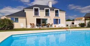 A two-story house with a swimming pool, outdoor furniture, and a patio area.