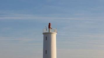 Un faro con cielo despejado, ubicado en un campo cubierto de hierba y algunas personas a lo lejos.