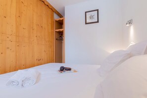 Une chambre d’hôtel avec une armoire en bois, un lit avec du linge de maison blanc, un tableau encadré au mur et une lampe de chevet.
