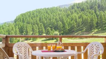 Une terrasse en bois avec une table et des chaises, une carafe de jus d’orange et une assiette de pâtisseries.