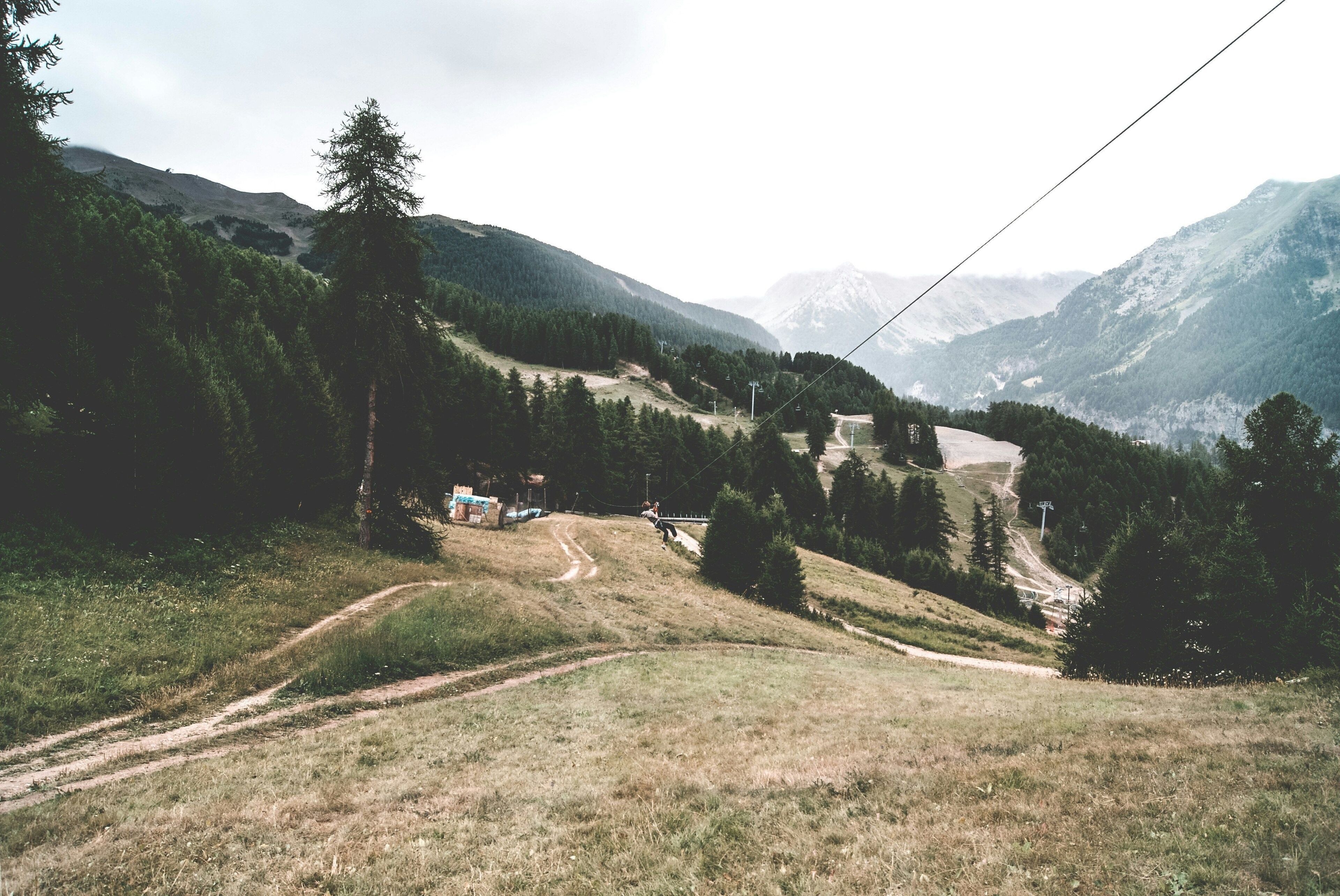 Un paysage montagneux avec un sentier de terre menant à un petit bâtiment entouré d’arbres.
