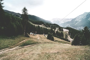 Un paysage montagneux avec un sentier de terre menant à un petit bâtiment entouré d’arbres.