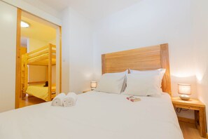 A hotel room with a wooden headboard, a bed with white linens, two bedside lamps, and a wooden nightstand.