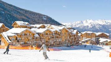 Une station de ski avec des chalets en bois, une piste de ski et, en arrière-plan, des montagnes enneigées.