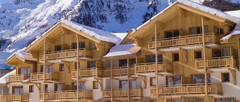 A wooden chalet with multiple balconies and a snow-covered mountain backdrop.