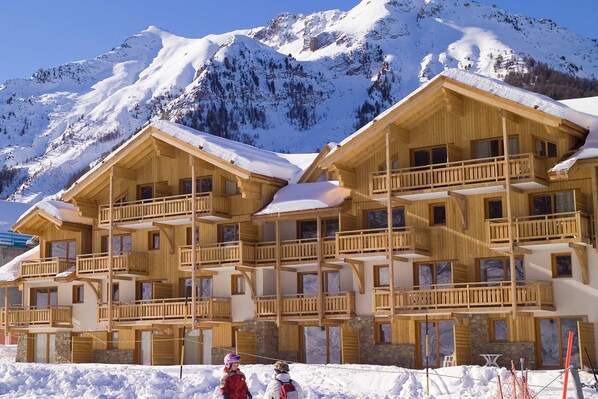 A wooden chalet with multiple balconies and a snow-covered mountain backdrop.