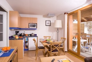 Cozinha compacta com armários de madeira, micro-ondas e área de refeições com mesa e cadeiras.