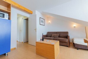 Ein gemütlicher, kompakter Wohnbereich mit einem Holztisch, einem braunen Sofa, einem Bett und einer Küchenzeile inklusive Mikrowelle.