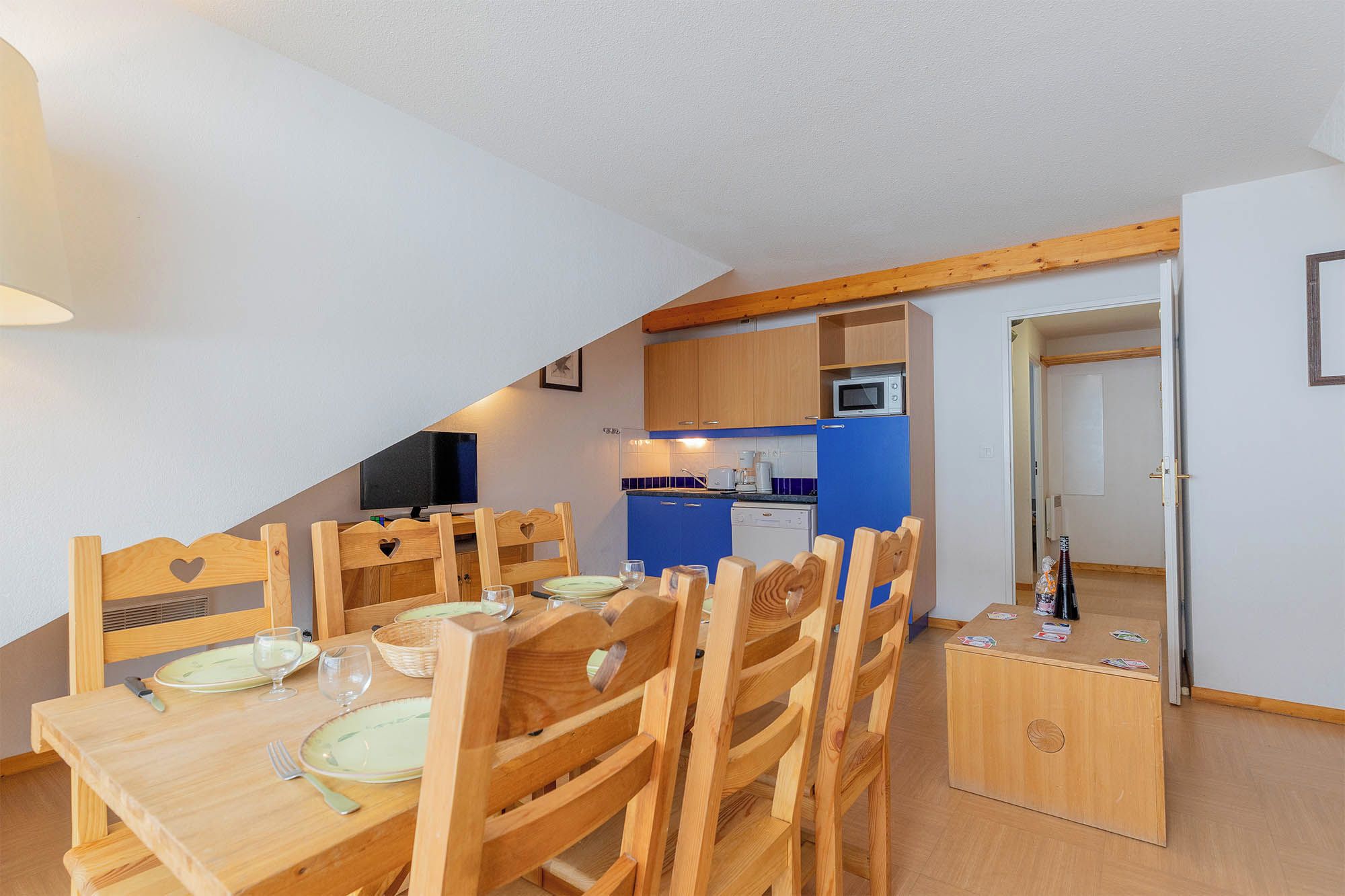 Ein Essbereich mit Holzkästen und einem Tisch für vier Personen, eine Küche mit blauen Schränken und einer Mikrowelle sowie eine Tür zu einem anderen Raum.