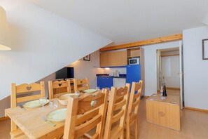 A dining area with wooden chairs and a table set for four, a kitchen with blue cabinets and a microwave, and a door leading to another room.
