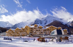 Una località montana innevata con edifici in legno, una seggiovia e una cabinovia.