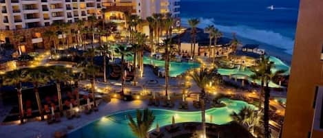 A resort with multiple swimming pools, palm trees, and a beachfront view.