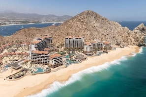 Ein Küstenresort mit mehreren Gebäuden, einem Sandstrand und einem felsigen Berg im Hintergrund.