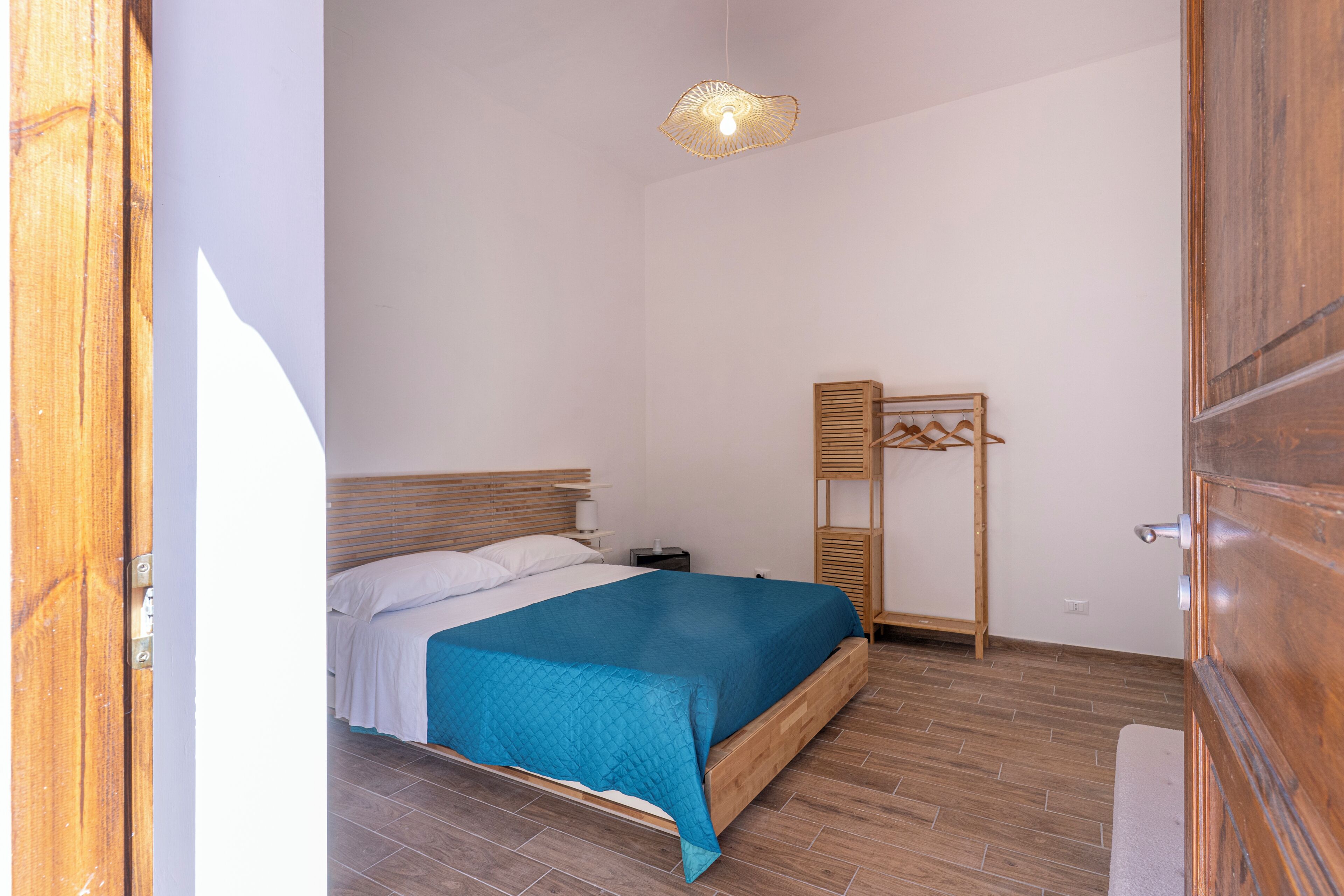 A bedroom with a bed, a bedside table, a hanging light fixture, and a wooden wardrobe.