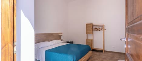 A bedroom with a bed, a bedside table, a hanging light fixture, and a wooden wardrobe.
