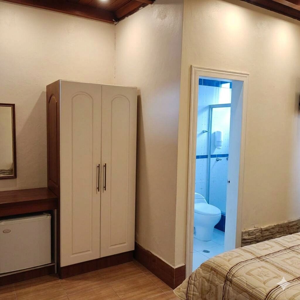 A bedroom with a bed, a wardrobe, a small table, and a door leading to a bathroom.