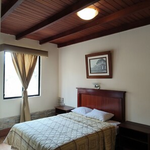 Un dormitorio con cama, mesita de noche, cuadro en la pared y ventana con cortinas.
