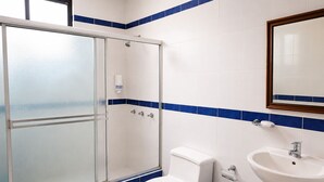 Un baño con cabina de ducha de vidrio, inodoro, lavamanos y un cubo de basura azul.