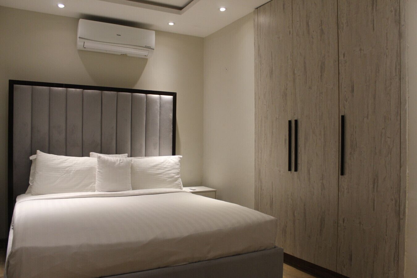 A modern bedroom with a bed, a nightstand, an air conditioning unit, and a wardrobe.