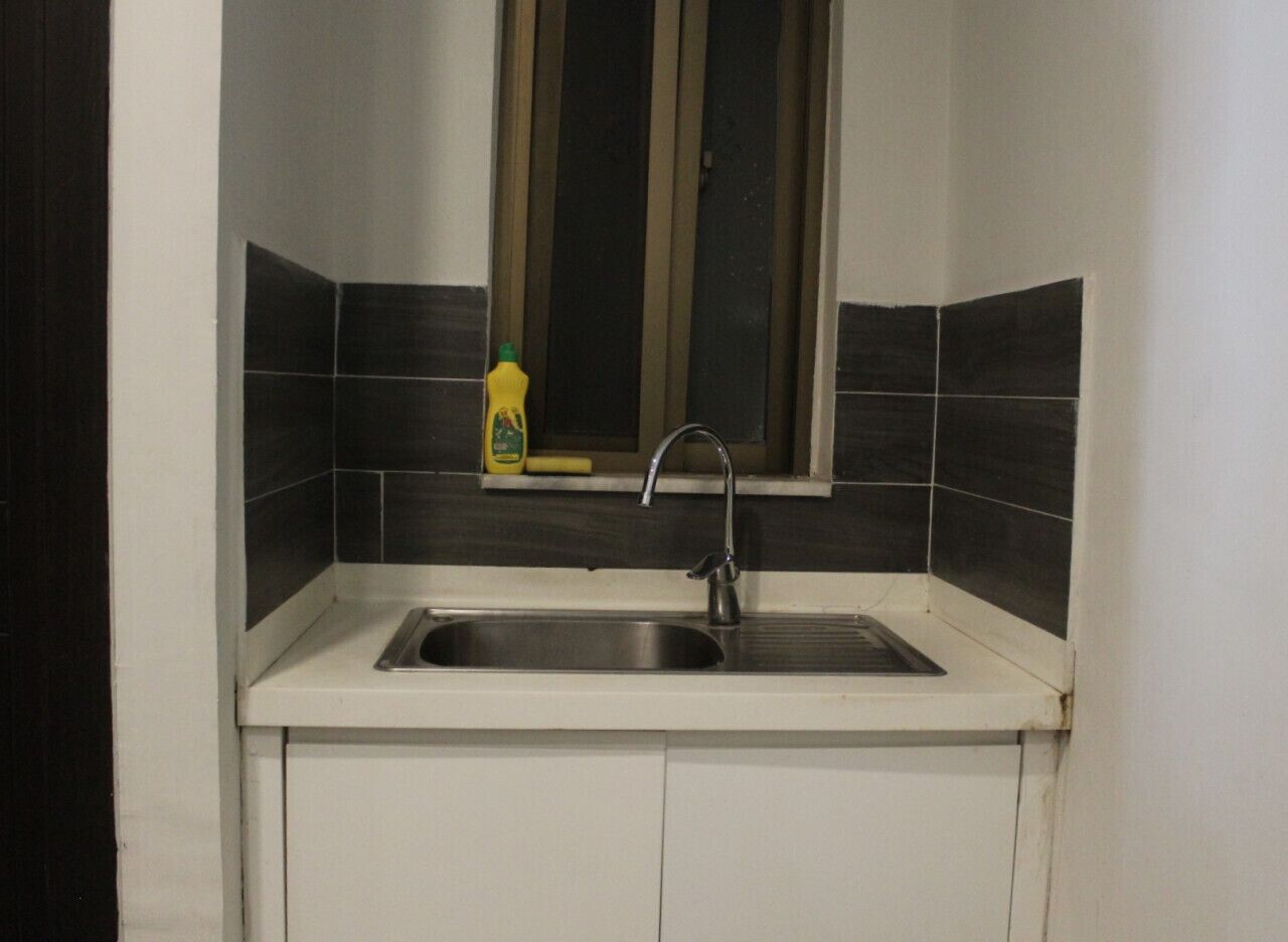 A kitchen with a stainless steel sink, a window above it, and a bottle of dish soap on the counter.