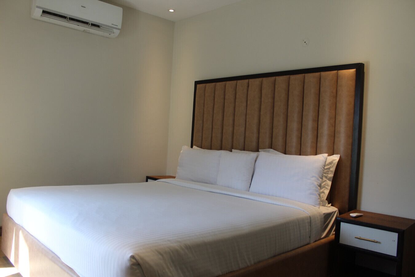 A hotel room with a large bed, a nightstand, a drawer, and an air conditioning unit on the wall.