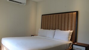 Ein Hotelzimmer mit einem großen Bett, einem Nachttisch, einer Schublade und einer Wandklimaanlage.