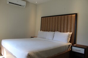 Et hotelværelse med en stor seng, et natbord, en skuffe og en aircondition på væggen.