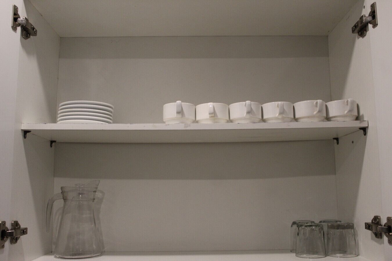 Un meuble blanc avec des étagères où sont rangées des assiettes, des tasses et un pichet.