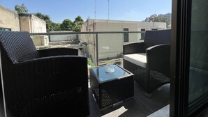 Ein Balkon mit Korbmöbeln und einem Glastisch mit Blick auf eine Stadtansicht.